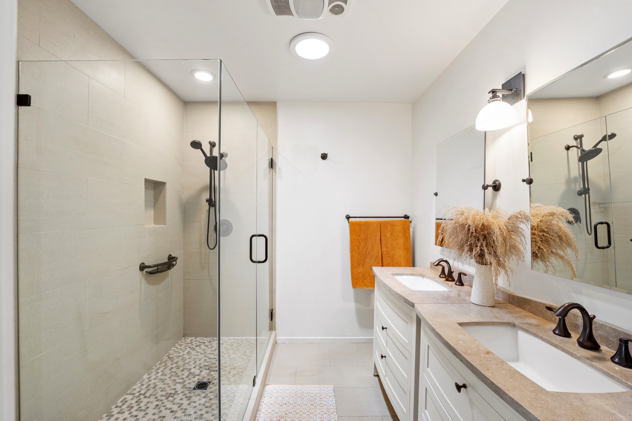 Spa bathroom with double stone vanity, glass walk-in shower with pebble floor, and pampas grass