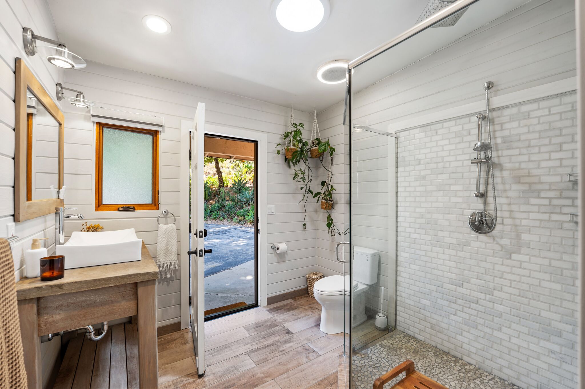 White shiplap bathroom with walk-in shower and the door open to the garden path