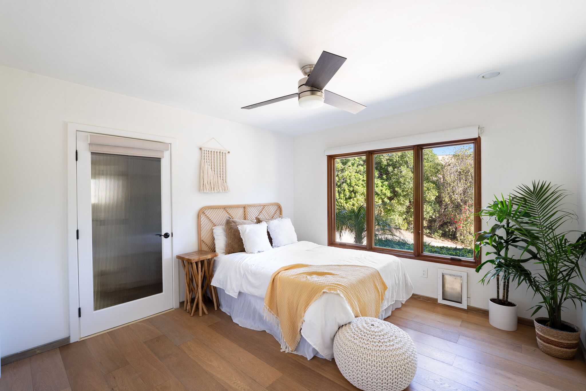 Bedroom with ceiling fan, woven bench, and windows onto the oaks