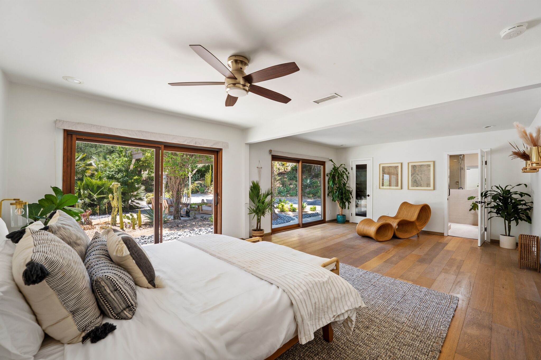 Wide primary bedroom with sliding garden doors, wicker lounger, and layered textile pillows