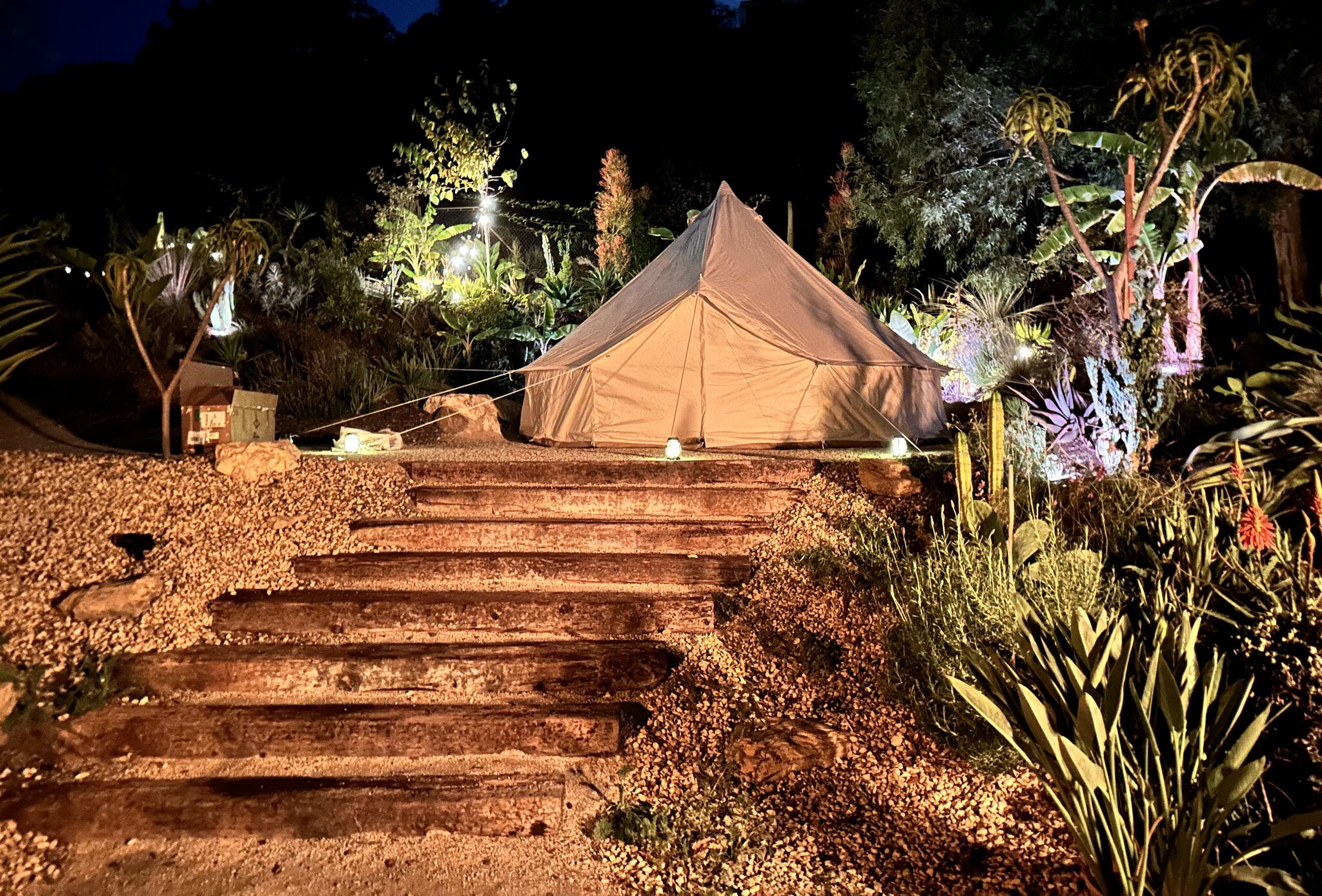 White bell tent glowing at dusk on the railroad-tie garden steps