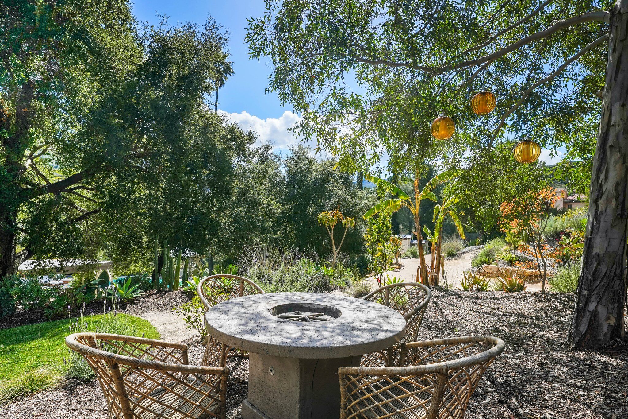 Stone fire-pit dining nook beneath oak trees hung with amber lanterns