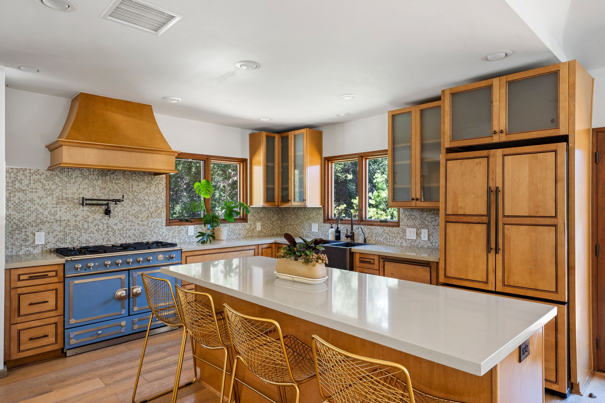 Chef’s kitchen with blue La Cornue range, copper hood, and gold counter stools at the island