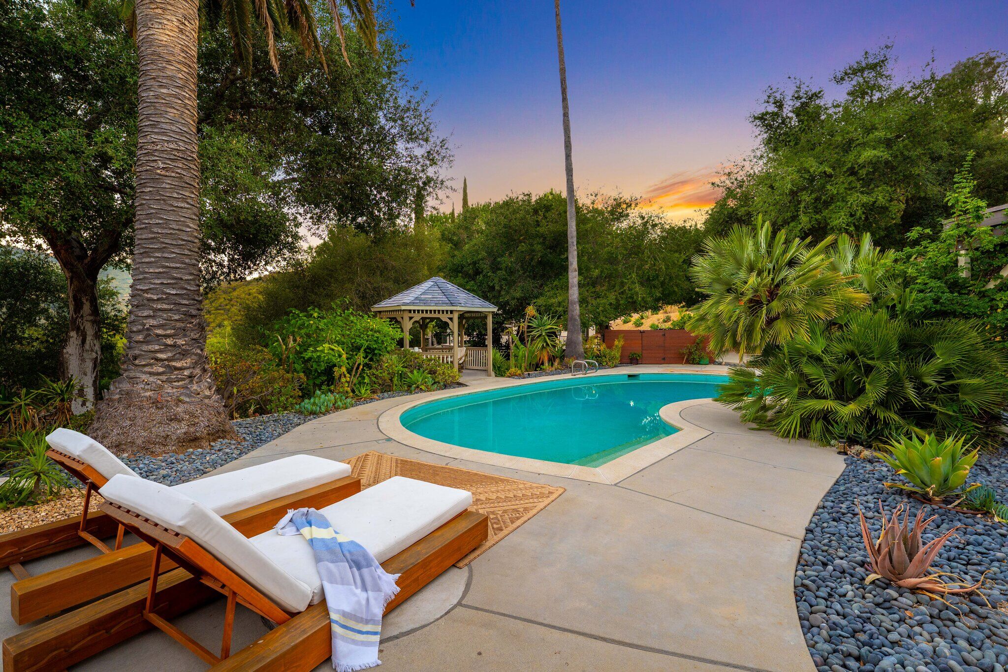 Saltwater pool at dusk with chaise lounges and the gazebo under a violet sky