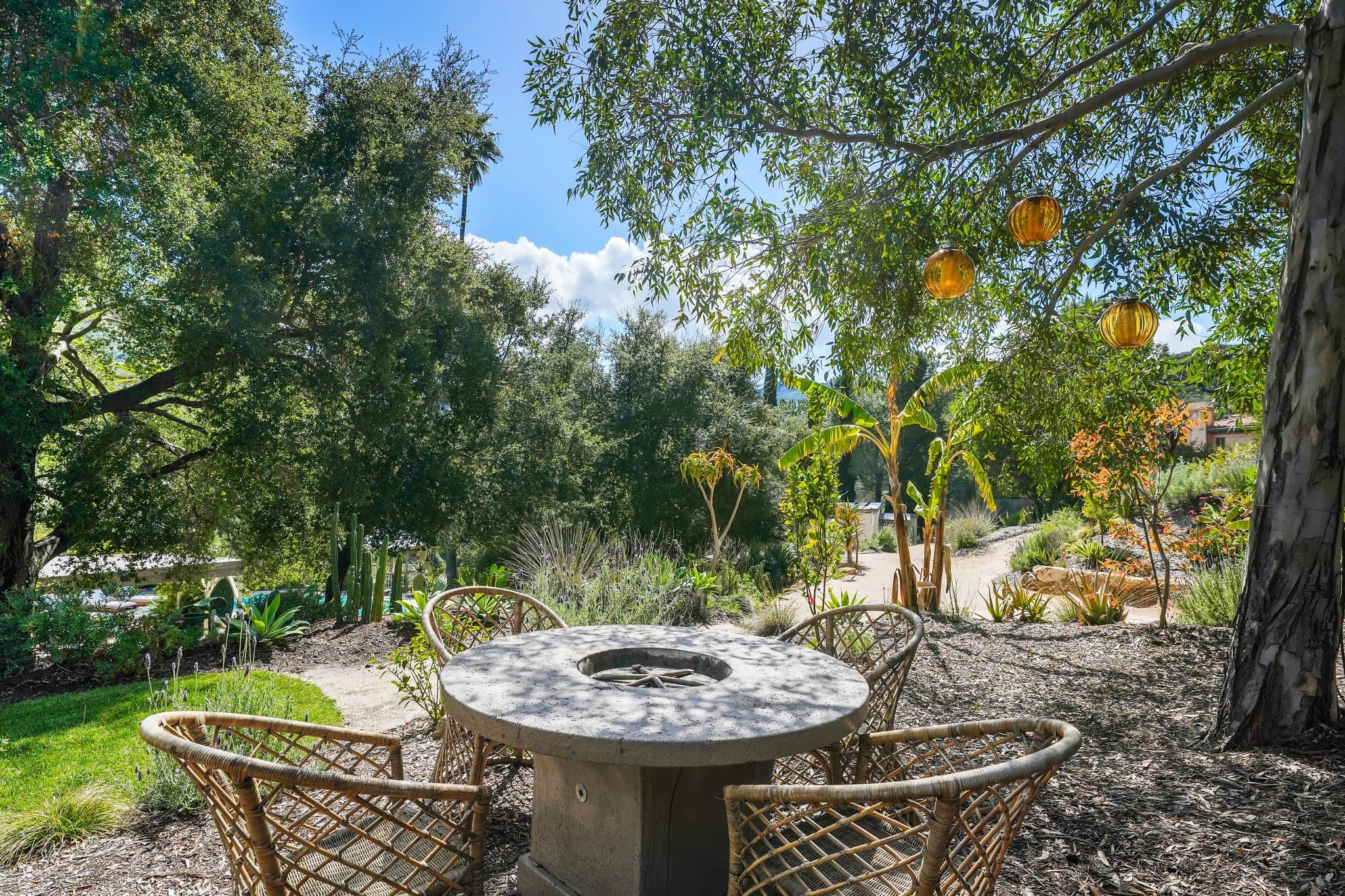 Stone fire-pit dining nook beneath oak trees hung with amber lanterns